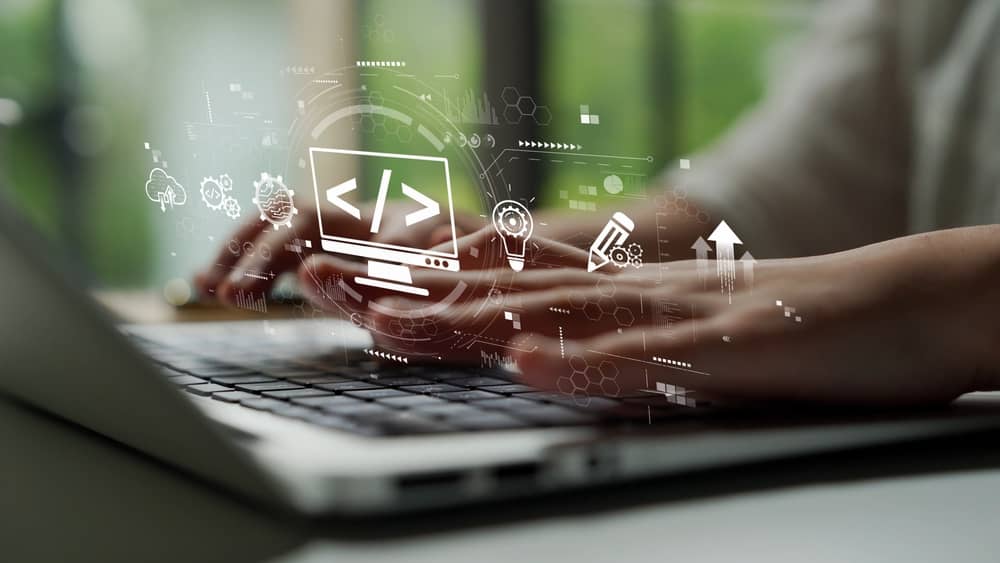 Manos escribiendo código en un portátil con iconos de desarrollo, representando qué es backend y cómo construirlo.